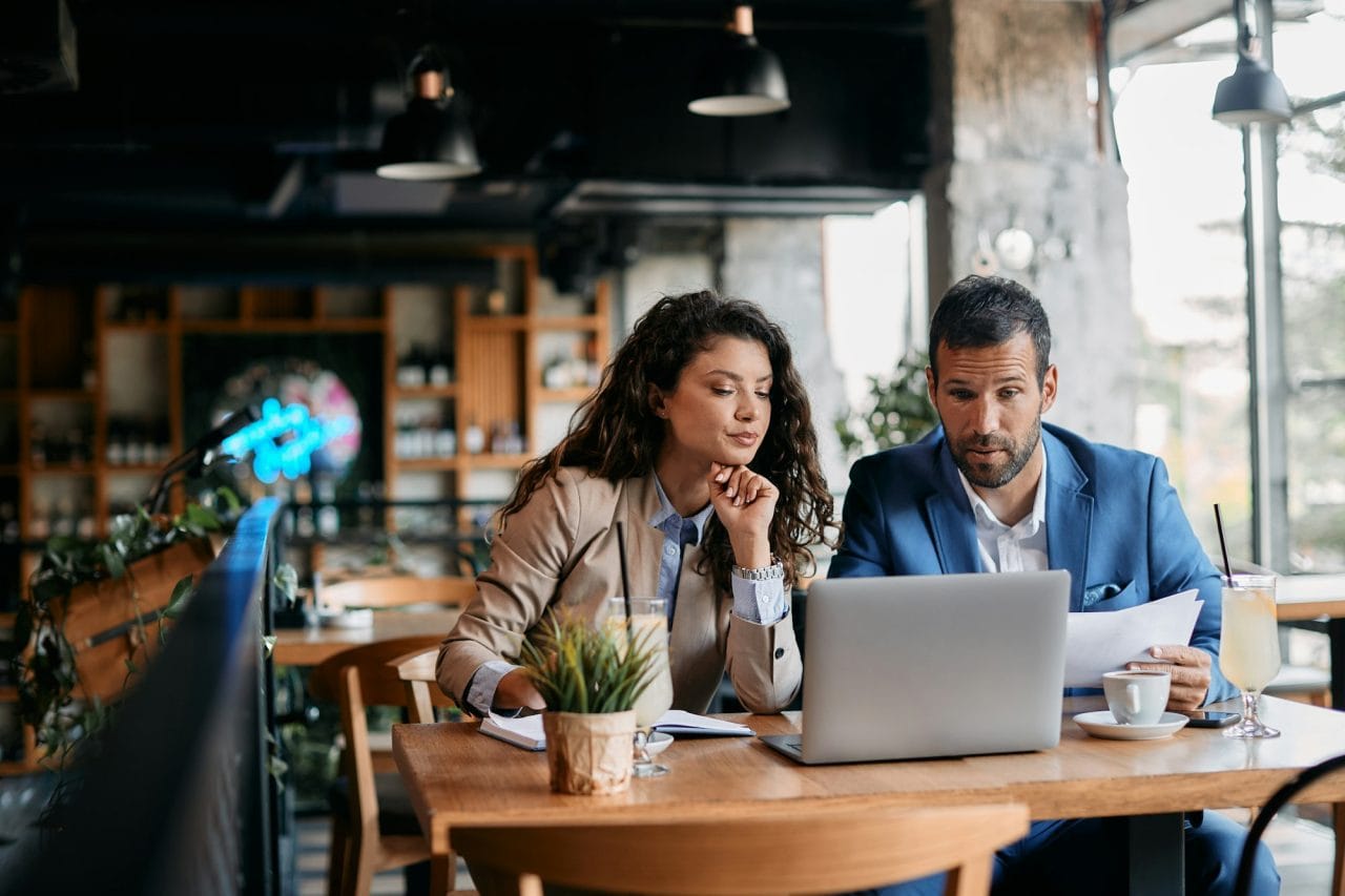 HypnoSemantic Marketing Agency providing Affordable Web Designing SEO PPC and Qualified Lead Generation in Toronto business colleagues using laptop and analyzing documents on a meeting in cafe